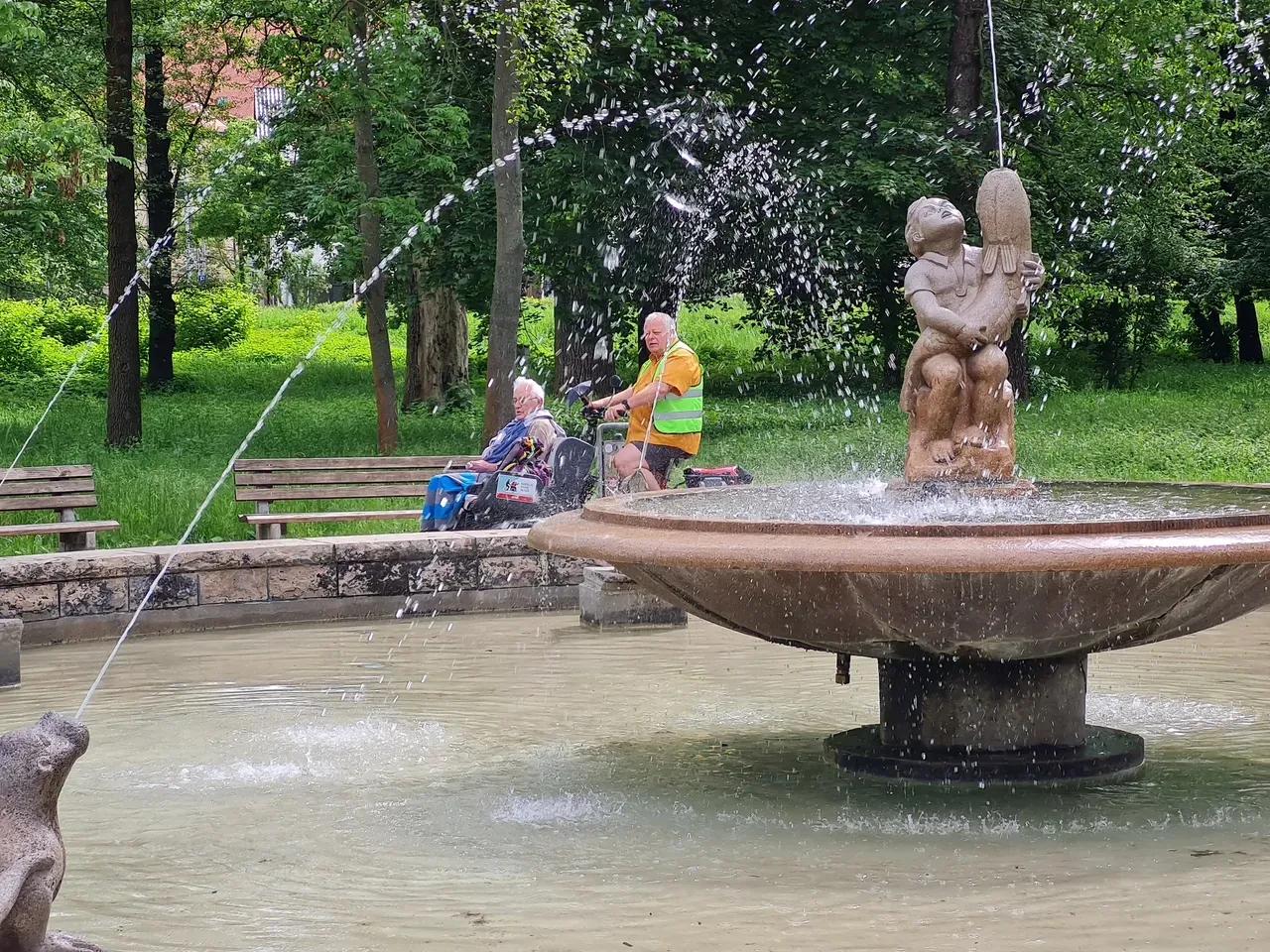 Brunnen in der Oberaue Jena, dahinter fährt eine Fahrradrikscha