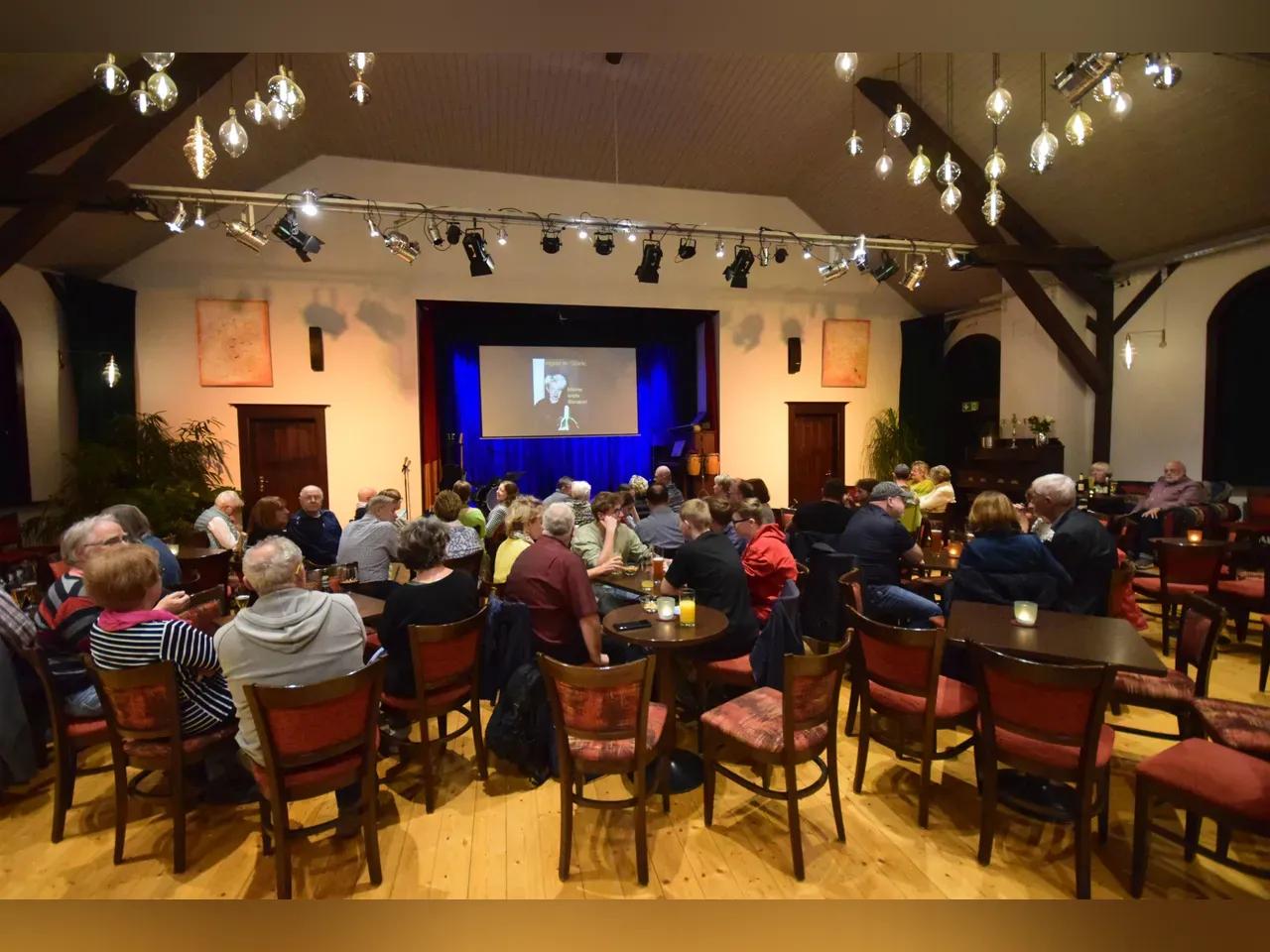 Bühnensaal mit Stühlen, Tischen und Publikum