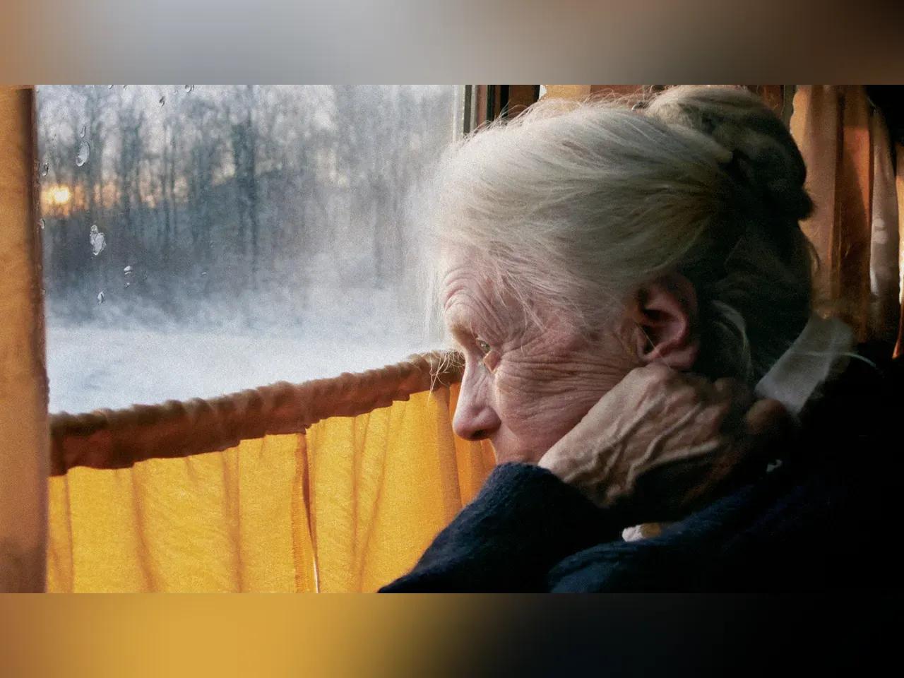 Eine ältere Dame mit weißem hochgestecken Haar schaut nachdenklich aus einem Fenster