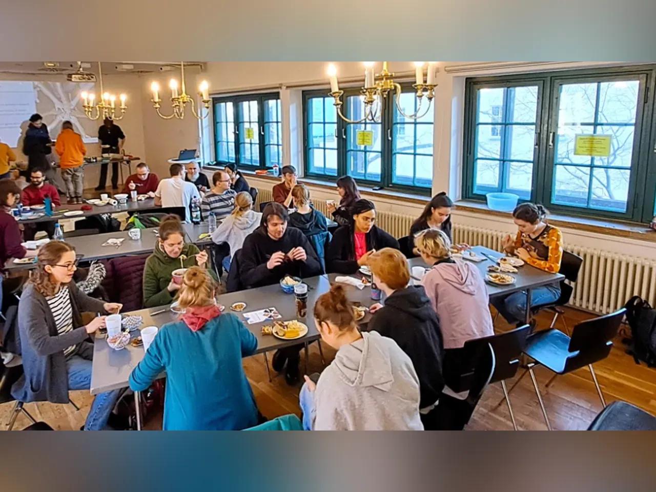 Mehrere Leute sitzen gemeinsam an Tischen und essen verschiedene Speisen. 