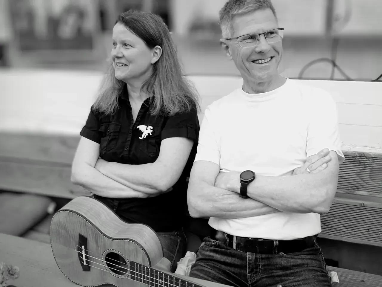 Schwarz-weiß Foto von einer Frau und einem Mann, die auf einer Bank sitzen, mit einer Ukulele auf dem Schoß