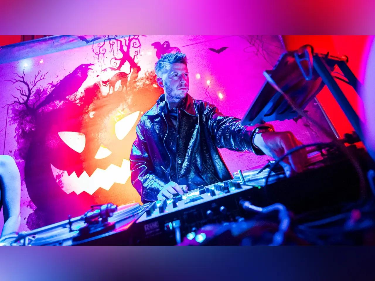 DJ am Pult, im Hintergrund Halloween-Dekoration
