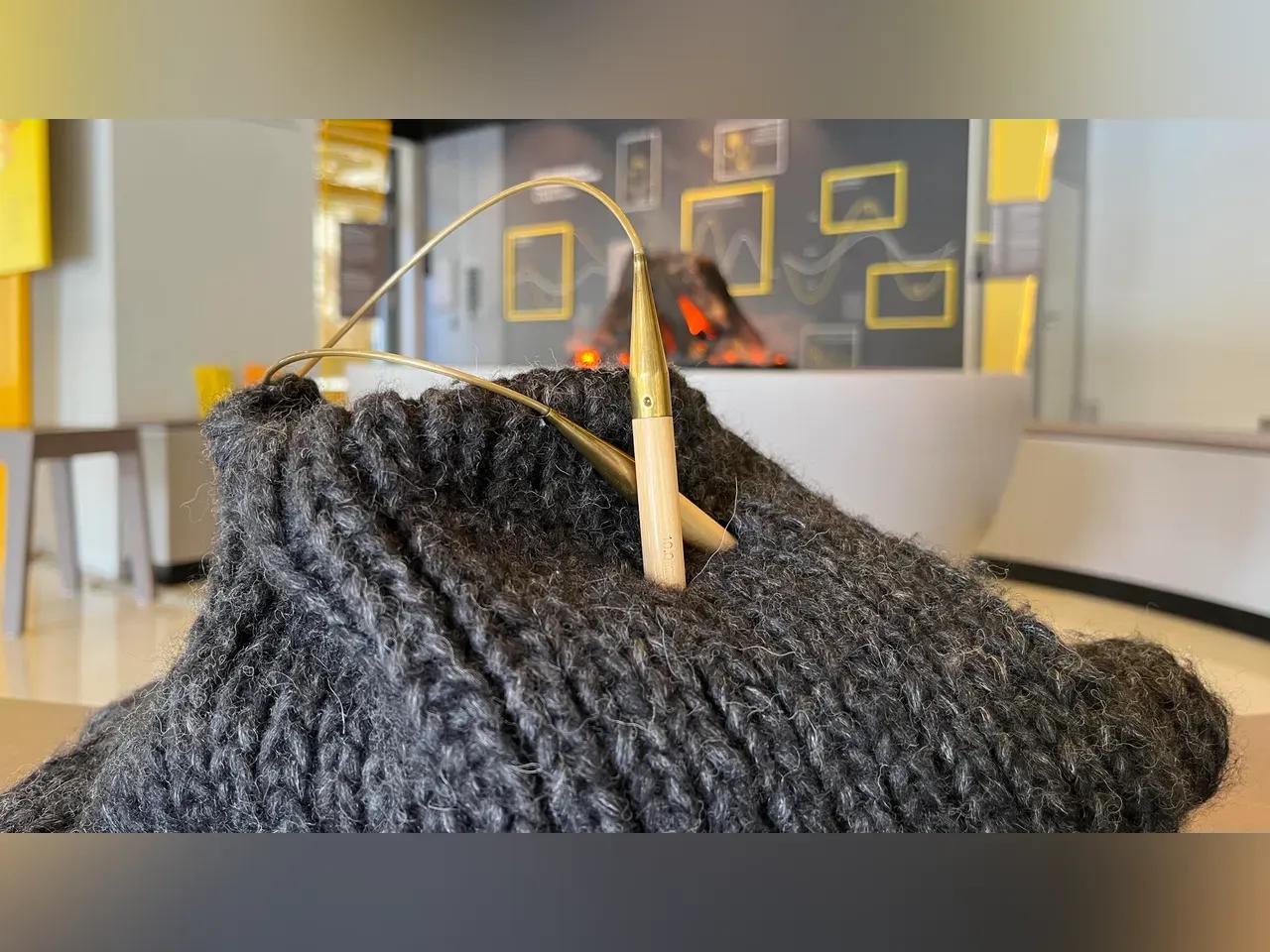 Strickteil aus grauer Wolle, in dem Nadeln stecken