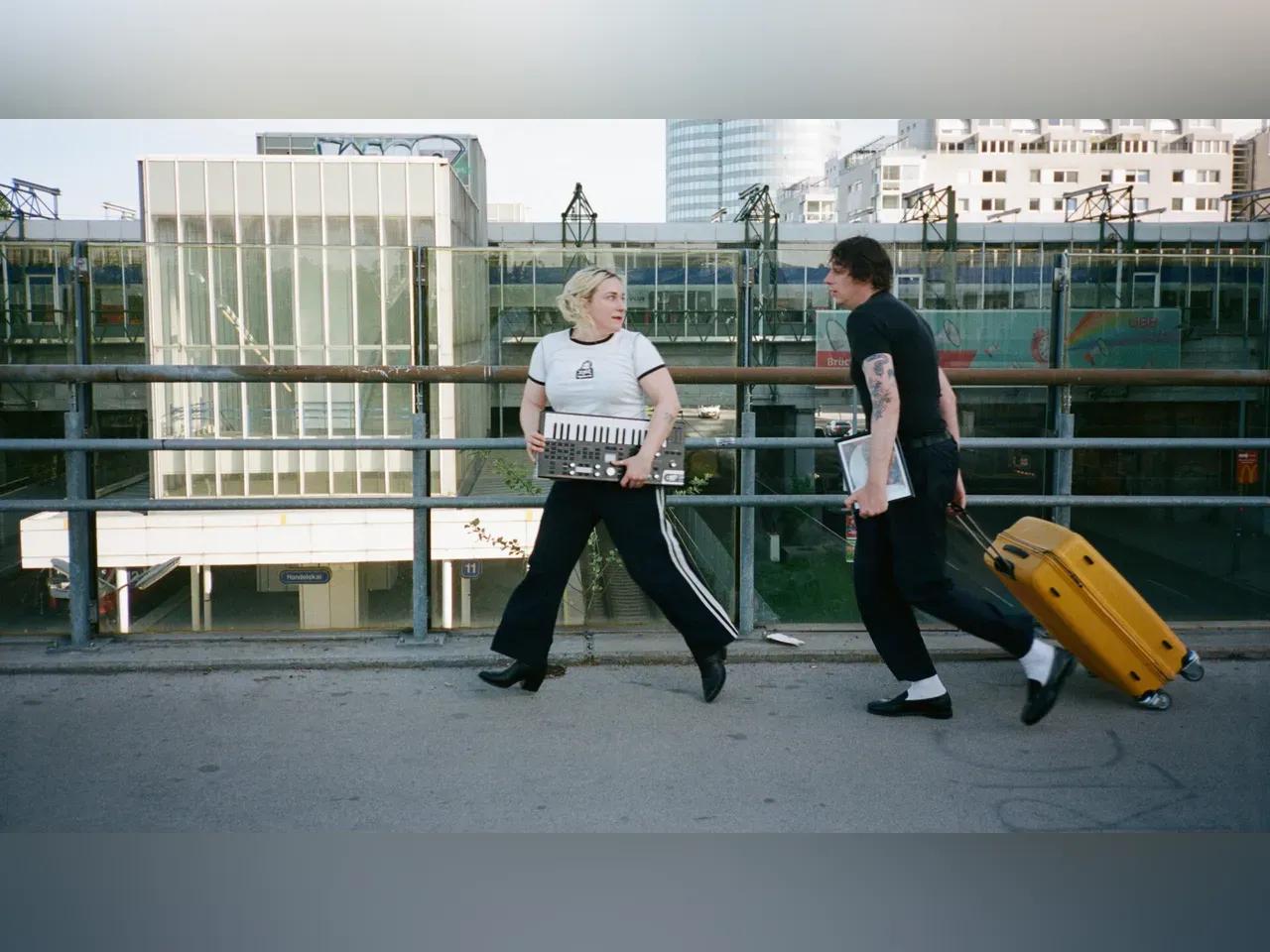 Die zwei Musiker:innen von EUROTEURO mit Instrumenten und Rollkoffer auf einem Gehweg
