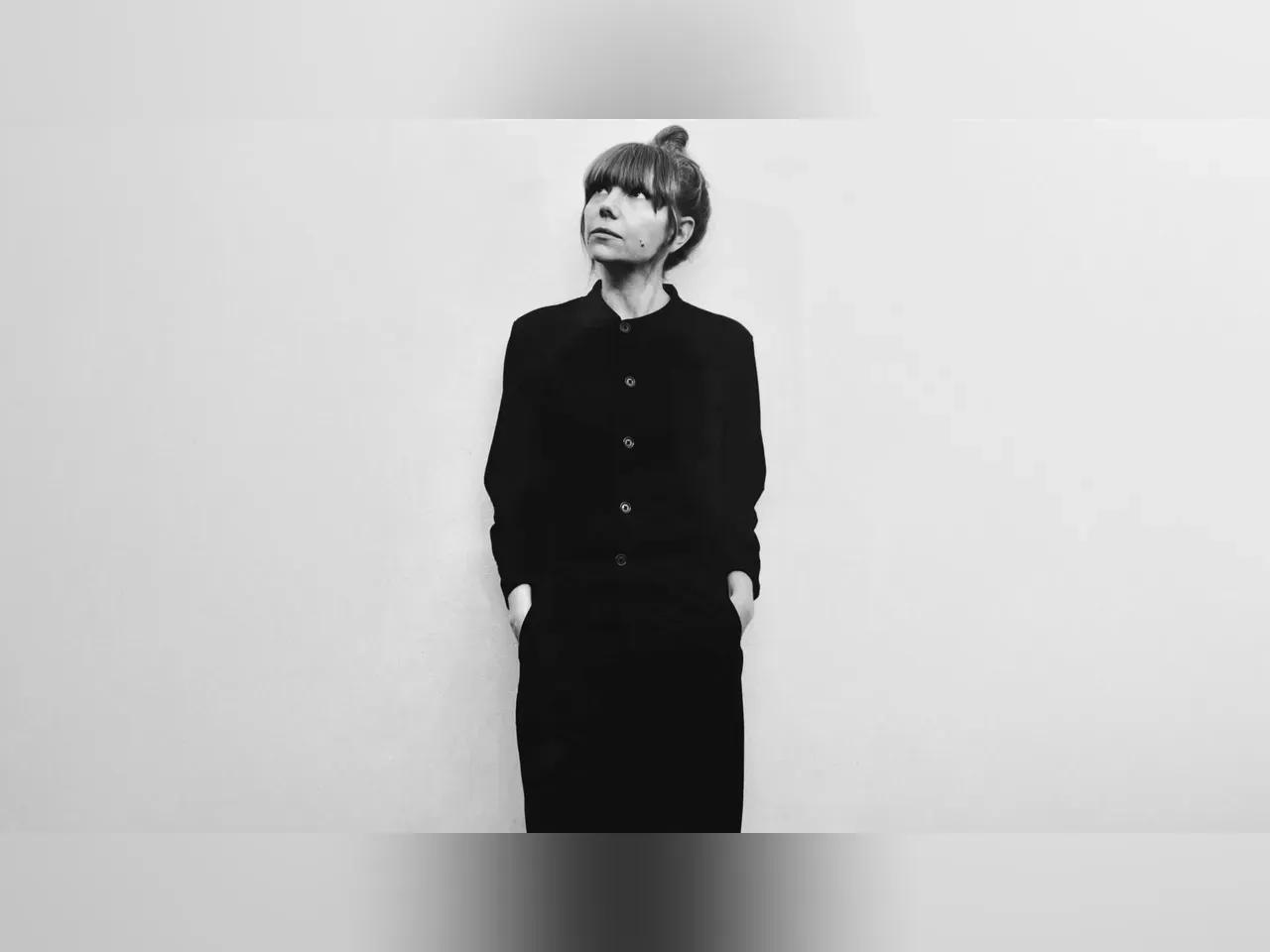 Schwarz-weiß Foto der Künstlerin Poppy Ackroyd, die an einer hellen Wand lehnt