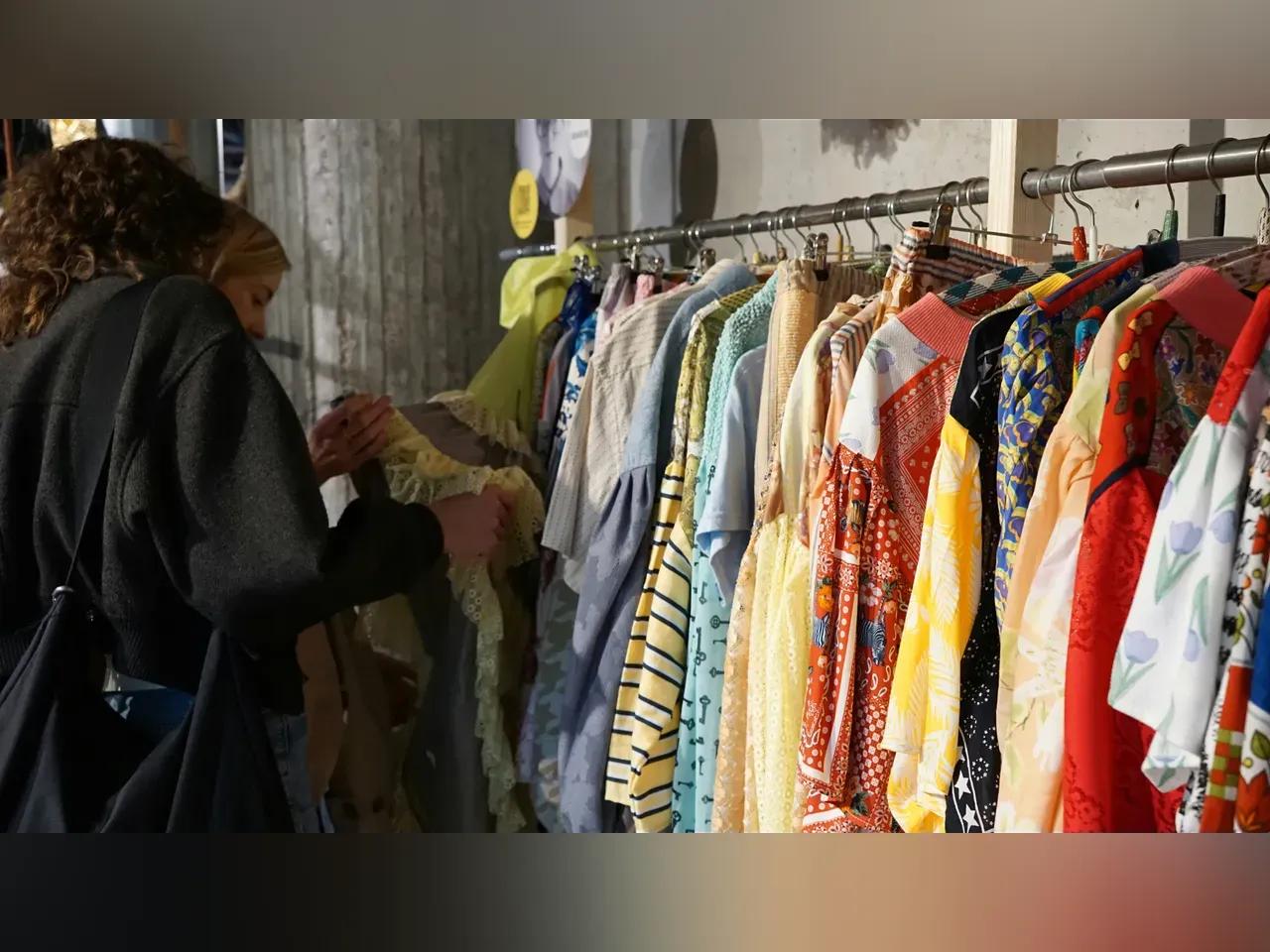 Kleiderstange mit vershiedenen Kleidungsstücken und zwei Menschen, die die Kleidung anschauen