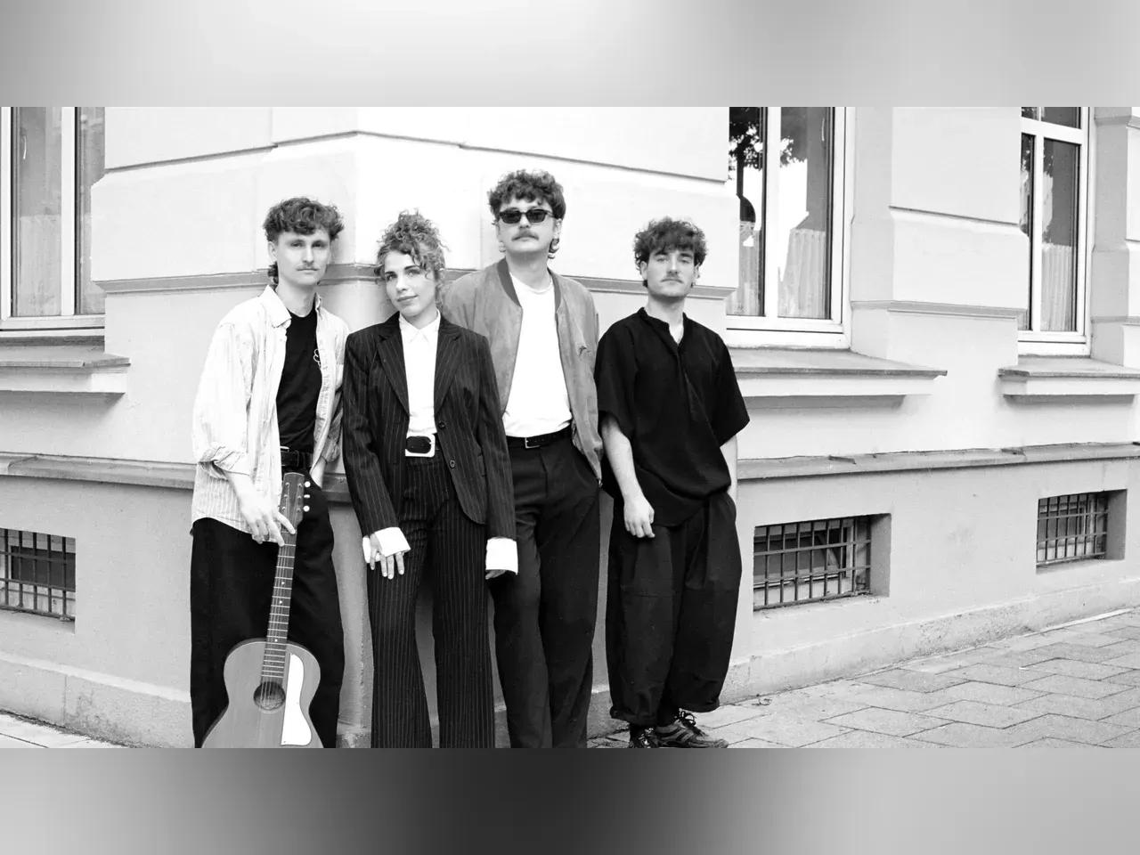 Schwarz-Weiß-Gruppenbild von vier Musiker:innen an einer Häuserecke